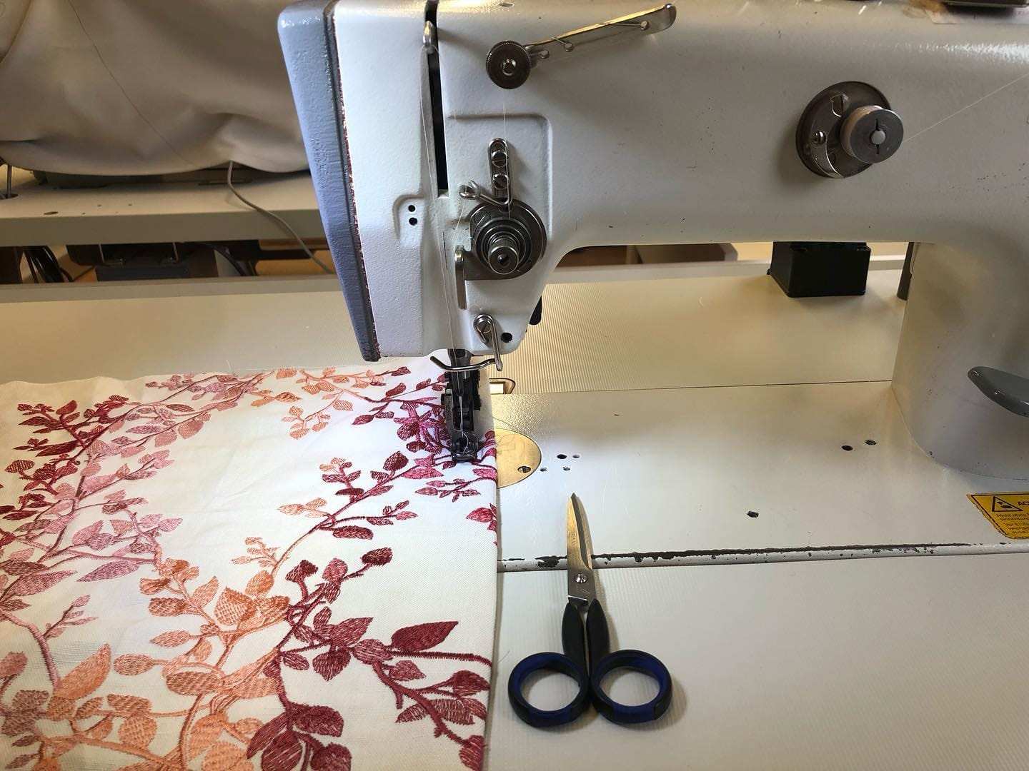 Bestickter Stoff an der Industrienähmaschine, daneben die Schere